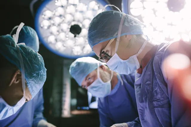 Chirurgi cu măști și bonete, operând sub lămpile unei săli de operație