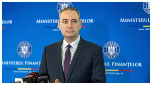 Bărbat în costum, la o conferință de presă, în fața panoului Ministerului Finanțelor