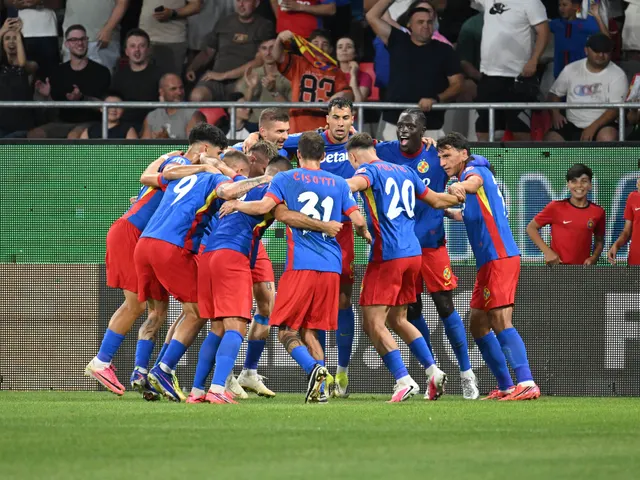 Fotbaliști în tricouri roș-albastre îmbrățișați în grup pe teren, în fața tribunei