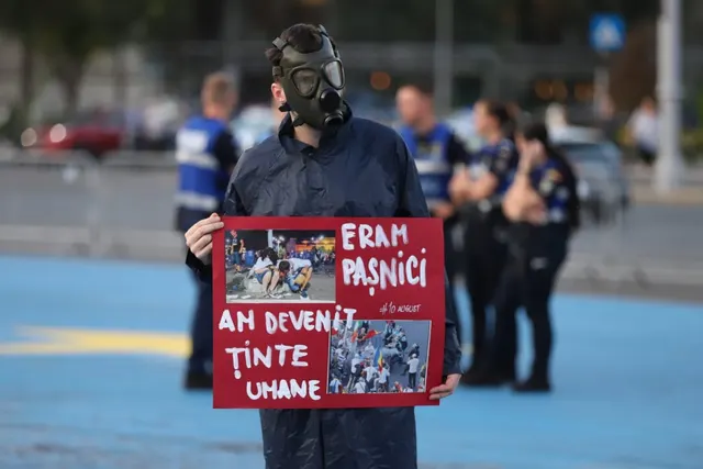 Protestatar cu mască de gaze și pancarta „Eram pașnici, am devenit ținte umane”, cu forțe de ordine în spate