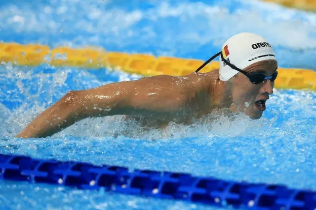 Vlad Mihalache înotând fluture, cu casca albă cu tricolor, într-un bazin cu culoare galbene