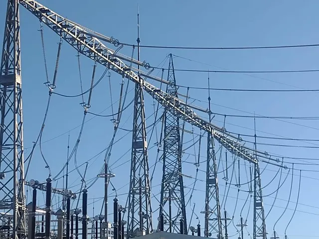 Stâlpi metalici de înaltă tensiune și rețele de cabluri dintr-o stație electrică, pe cer albastru