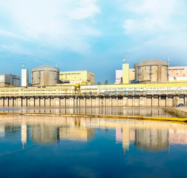 Reactoarele unei centrale nucleare oglindite în apa unui canal, sub un cer albastru cu nori