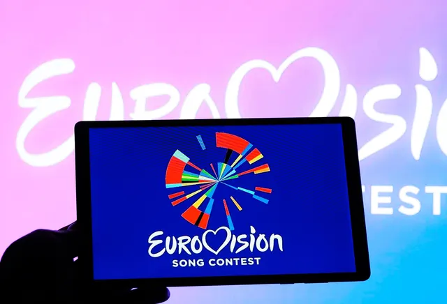 Sigla Eurovision Song Contest pe o tabletă, în fața unui fundal roz cu numele concursului