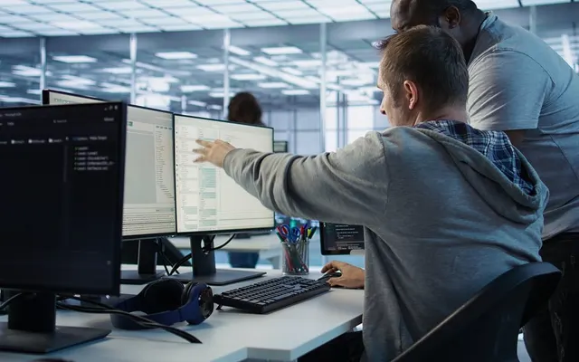 Angajați lucrând la birouri cu mai multe monitoare, într-un open space