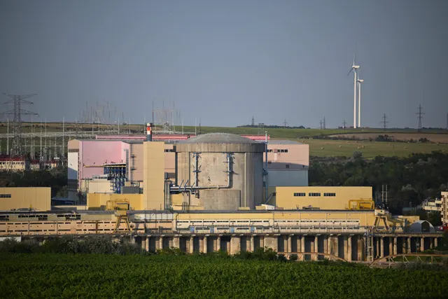 Centrală nucleară cu clădiri de reactor, o turbină eoliană în depărtare și un lan verde în față