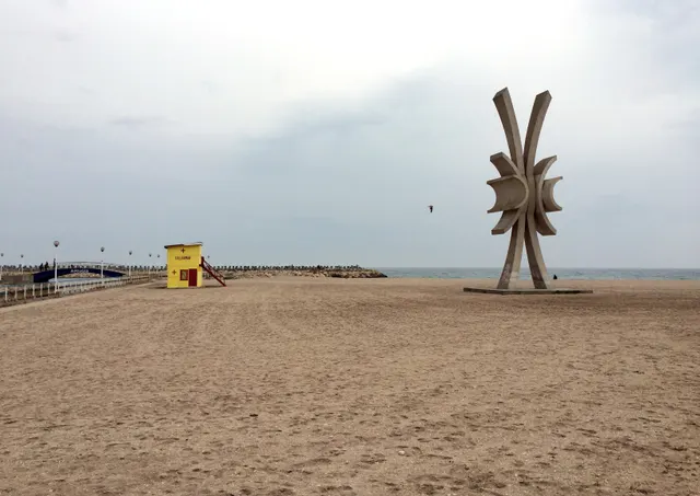 Plajă pustie cu un turn de salvamar galben și o sculptură metalică în formă de stea