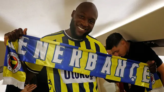 Fotbalist zâmbind în tricoul galben-bleumarin al lui Fenerbahçe, ținând un fular cu numele clubului