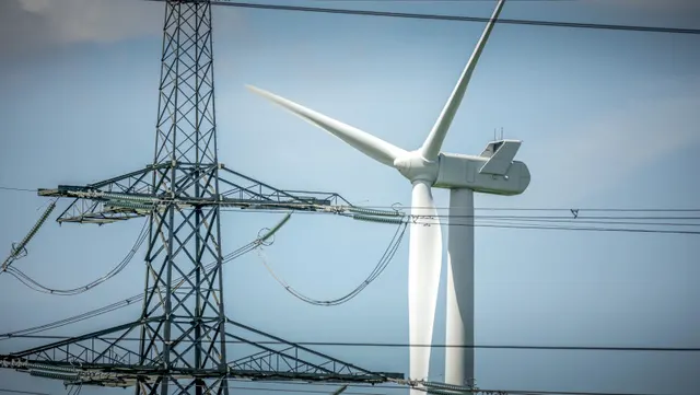 Turbină eoliană lângă un stâlp de înaltă tensiune, sub cer înnorat