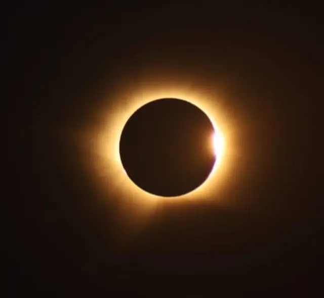 Eclipsă totală de Soare: discul negru al Lunii, înconjurat de coroana solară și un punct de lumină