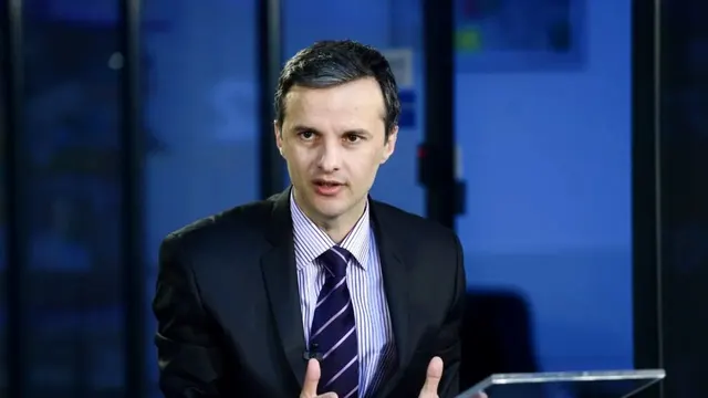 Cristian Socol, în costum și cravată în dungi, gesticulând în timp ce vorbește