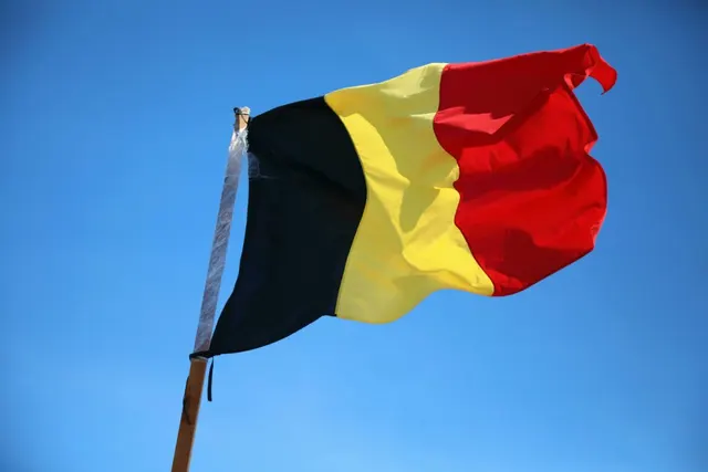 Drapelul Belgiei fluturând pe un catarg, pe cerul albastru