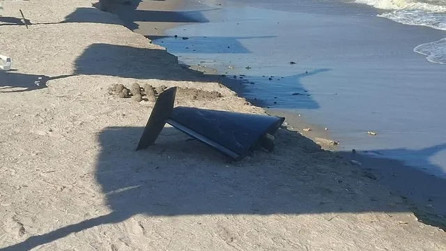 Epava unei drone căzute pe nisipul unei plaje, lângă linia apei
