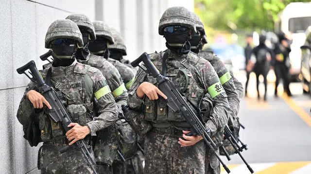 Militari cu cagule, ochelari și căști, înarmați cu puști, patrulând pe o stradă