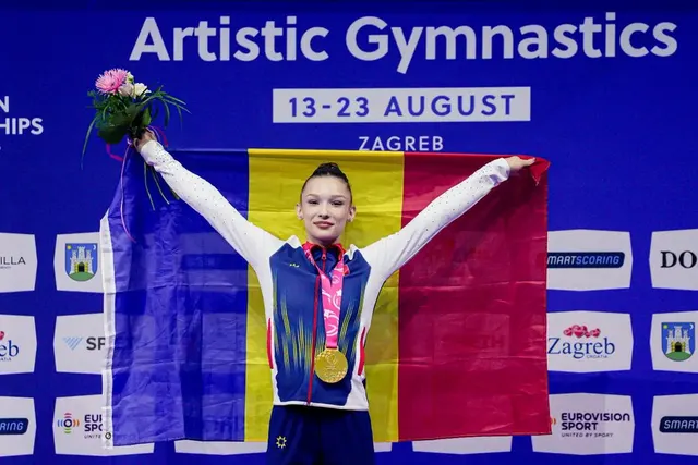 Gimnastă cu medalie, ținând drapelul României și un buchet de flori, sub panoul „Artistic Gymnastics, Zagreb”