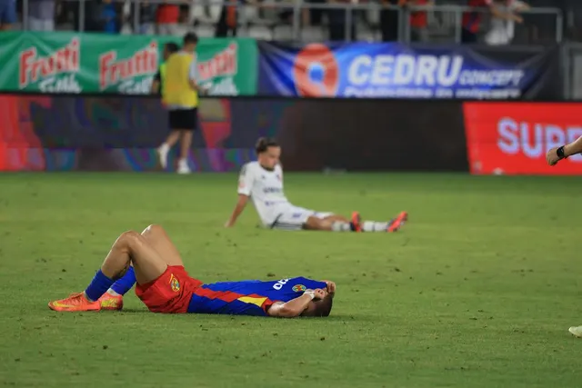 Fotbalist întins pe gazon, cu fața acoperită de mâini, iar un altul așezat în fundal