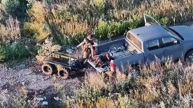Vedere de sus, filmată de o dronă: un militar lângă o camionetă civilă, într-o zonă cu iarbă și resturi