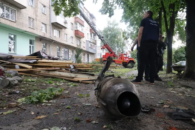 Resturile unei drone căzute lângă un bloc, printre moloz, cu un om în uniformă și o autospecială de pompieri