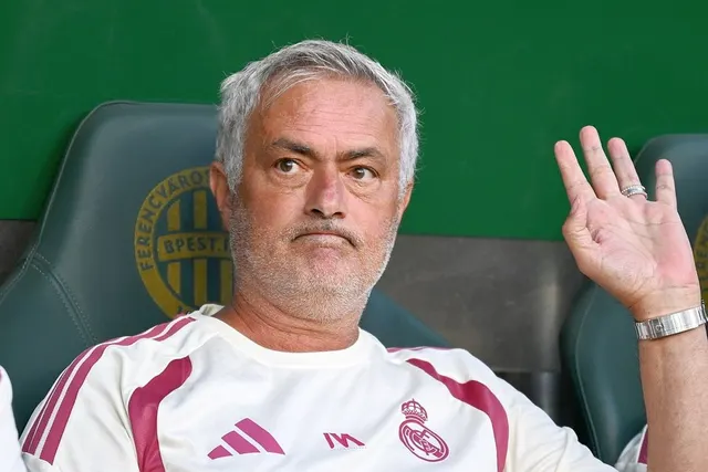 Bărbat cu părul cărunt, în bluză sport albă, ridicând mâna, așezat pe un scaun verde de stadion