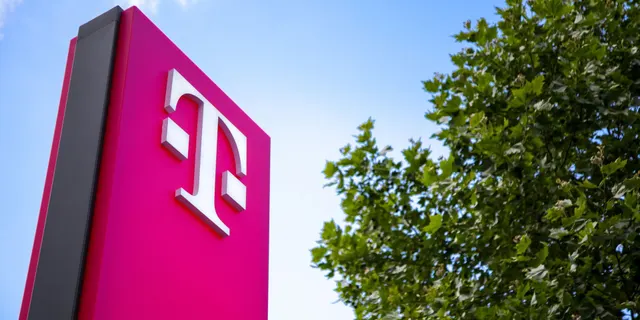 Totemul magenta cu sigla „T” a Deutsche Telekom, lângă un copac, pe cer albastru