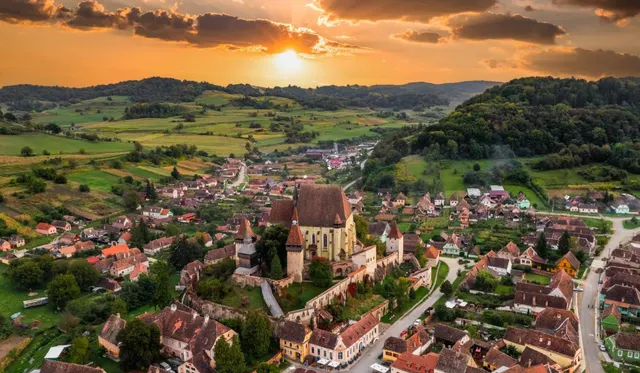 Sat din Transilvania cu o biserică fortificată pe deal, văzut de sus la apus