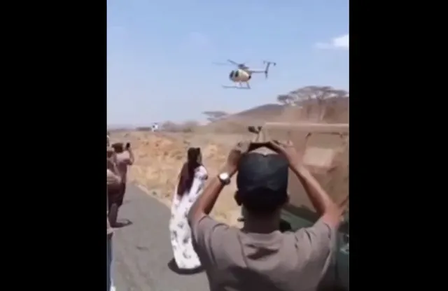 Captură video: oameni care filmează cu telefoanele un elicopter ce zboară jos deasupra unei câmpii
