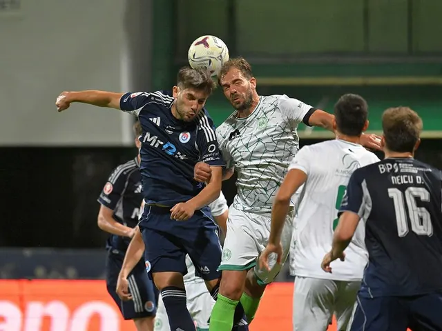 Fotbaliști sărind la o minge cu capul: unii în echipament bleumarin, alții în alb cu verde
