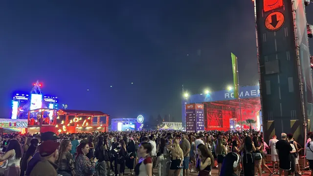 Mulțime de oameni la un festival în aer liber, noaptea, cu scene luminate
