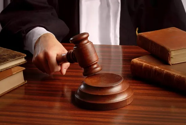 Mână de judecător cu un ciocănel deasupra unei mese de lemn, lângă cărți legate în piele