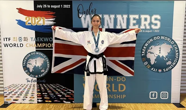 Sportivă în dobok alb, cu medalie, ținând drapelul Marii Britanii la Campionatul Mondial ITF de Taekwon-do
