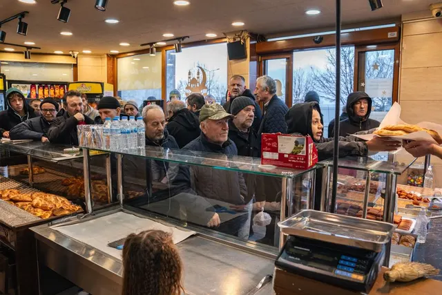 Clienți la coadă în fața vitrinei unei patiserii, cu produse de panificație pe tejghea