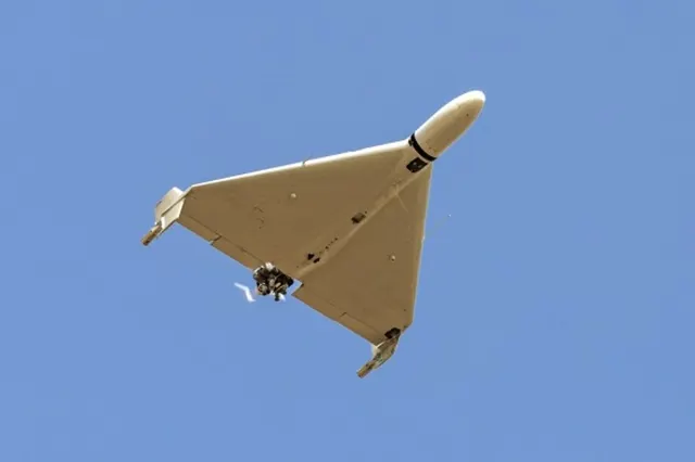 Dronă de culoare bej, cu aripi în delta și ampenaje verticale, în zbor