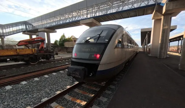 Tren de călători la peronul unei gări, sub o pasarelă pietonală