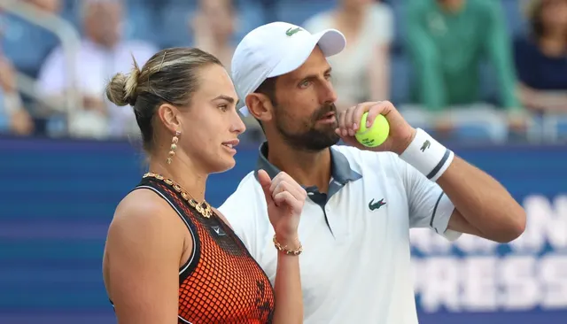 Jucătoare și jucător de tenis discutând pe teren; el poartă șapcă albă și ține o minge