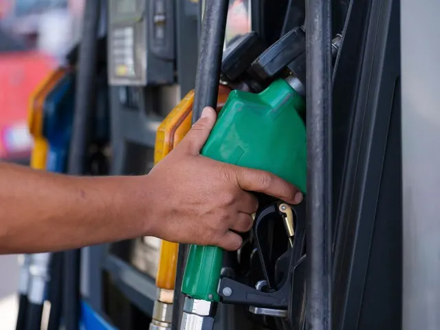 Mână care ține pistolul verde al unei pompe de carburant, la o benzinărie