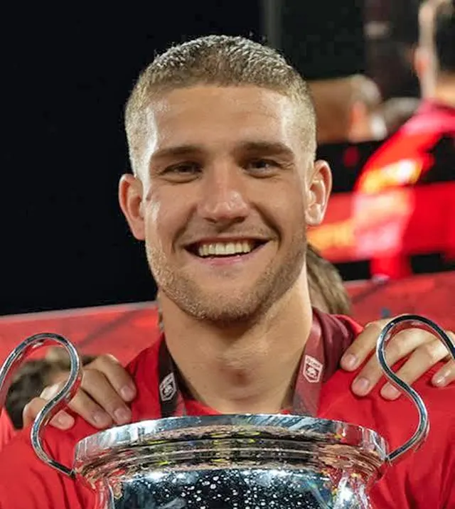 Tânăr fotbalist blond, zâmbind, cu un trofeu argintiu în mâini