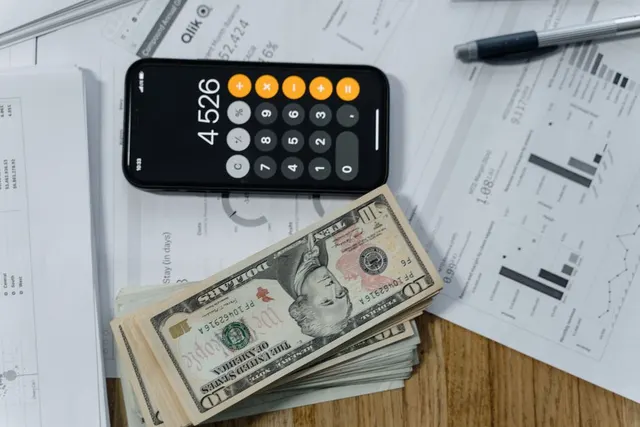 Calculator care afișează 4526, un teanc de bancnote de 100 de dolari și documente cu grafice