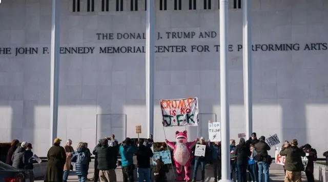 Protestatari cu pancarte în fața clădirii cu inscripția „The Donald J. Trump and The John F. Kennedy Memorial Center”