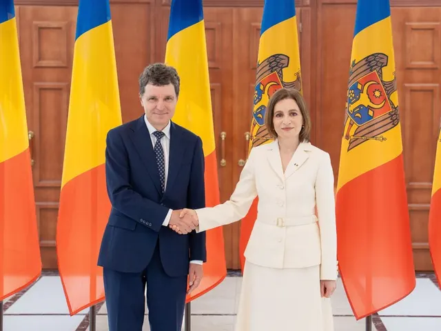 Bărbat în costum și femeie în costum alb dând mâna între drapelele României și Republicii Moldova