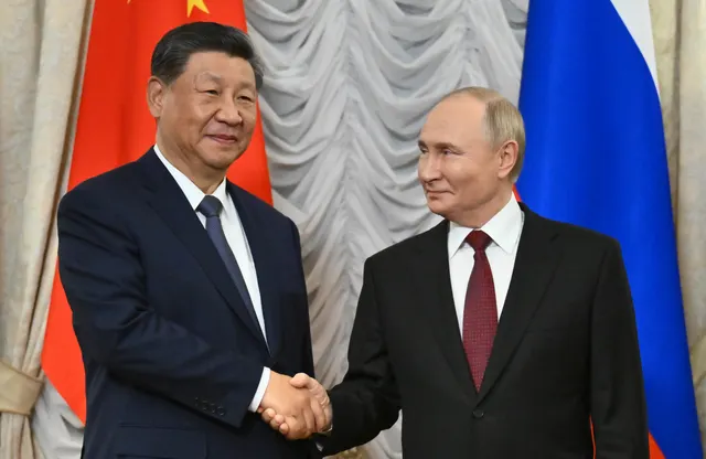 Doi bărbați în costume dând mâna în fața drapelelor Chinei și Rusiei