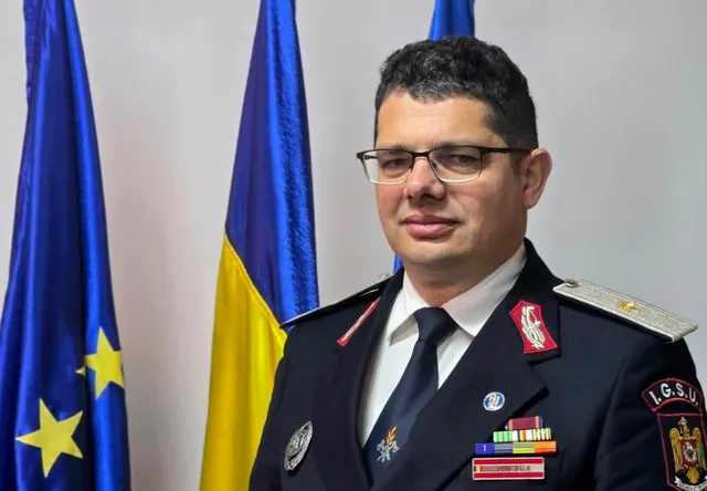 Ofițer cu ochelari, în uniformă de ceremonie IGSU cu decorații, între drapelele UE și României