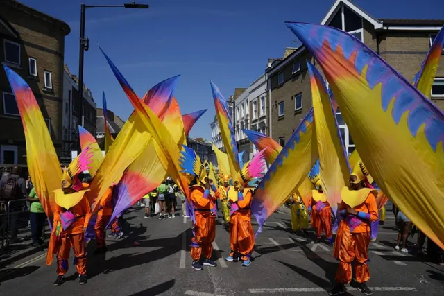 Dansatori în costume cu aripi colorate defilând pe o stradă, la un carnaval din Marea Britanie