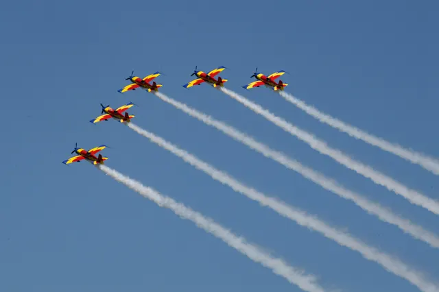Formație de avioane acrobatice roșu cu galben, cu dâre albe de fum pe cer albastru