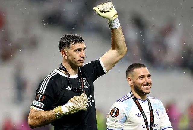 Portar în echipament negru ridicând pumnul, lângă un jucător zâmbitor în alb
