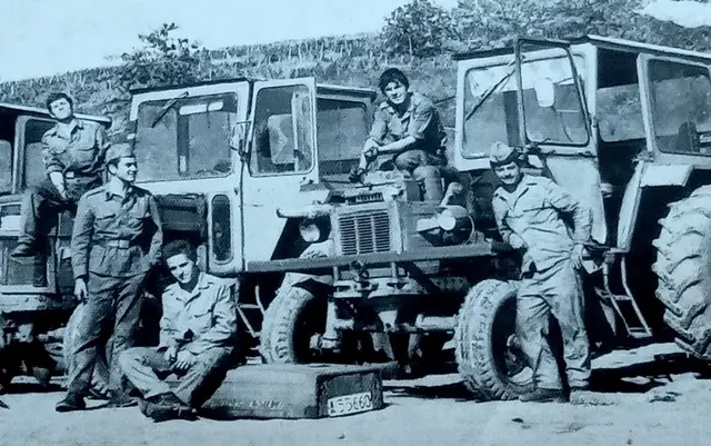 Militari în uniformă pozând lângă două camioane, într-o fotografie veche alb-negru