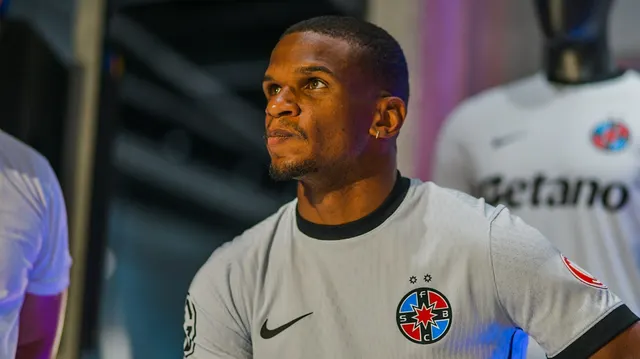 Fotbalist în tricou gri cu emblema FCSB, privind în sus, lângă tricouri expuse cu sponsorul „Betano”