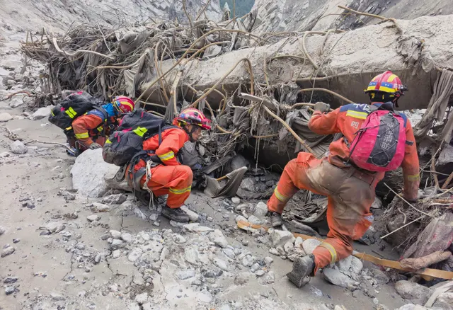 Salvatori în uniforme portocalii și căști, căutând printre dărâmături și noroi