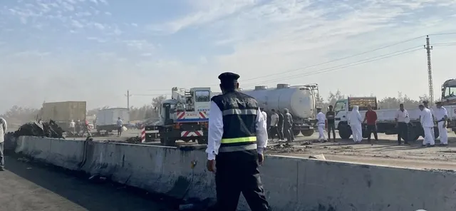 Polițist cu vestă reflectorizantă pe o șosea cu parapeți de beton, lângă camioane-cisternă și oameni adunați