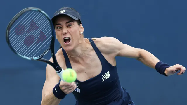 Jucătoare de tenis cu șapcă și echipament bleumarin, lovind mingea cu putere