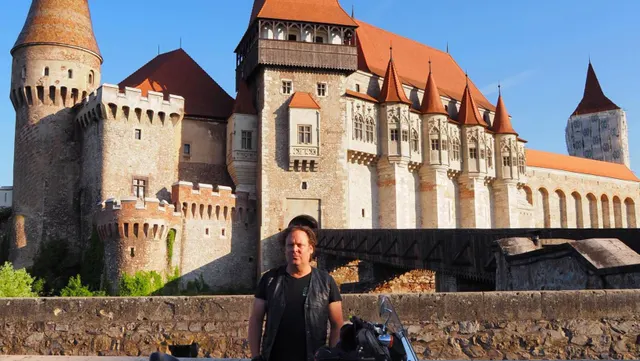 Bărbat în tricou negru în fața Castelului Corvinilor, cu turnurile și acoperișurile roșii